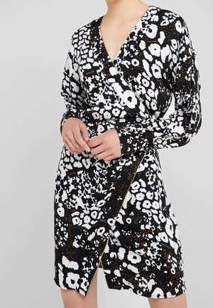 Czarna i biała sukienka kopertowa z mieszanką zwierzęcych wzorów i złotych akcentów, z długimi rękawami i głębokim dekoltem w serek. Gładka tekstura tkaniny.