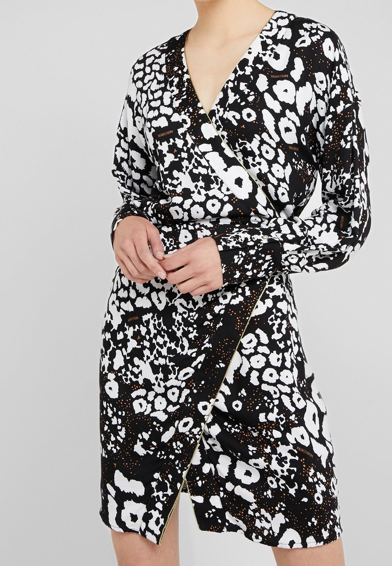 Robe portefeuille noire et blanche présentant un mélange d'imprimés animaliers avec des accents dorés, manches longues et un décolleté en V profond. Texture de tissu lisse.