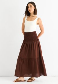 Weißer Bodysuit kombiniert mit einem braunen, gestuften Maxirock mit einem smockten Bund. Der Rock besteht aus leichtem, fließendem Material.