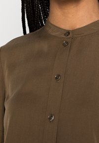 Camicia marrone a maniche lunghe realizzata in tessuto testurizzato, con colletto alla francese e due bottoni visibili sul profilo.