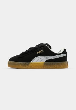 Black suede sneaker with white side stripe and gold logo. Features a rubber gum sole with textured pattern. Laces are black and flat.