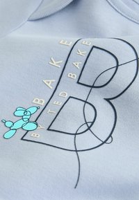 Lyseblå sweatshirt med et stort "B"-motiv i marineblå kontur, med gulddetaljer og en turkis ballonhund-illustration. Blød tekstur.