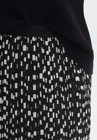 Gonna nera plissettata con un motivo astratto bianco. Vita elastica e tessuto testurizzato visibili, parzialmente coperti da un top a coste nero.