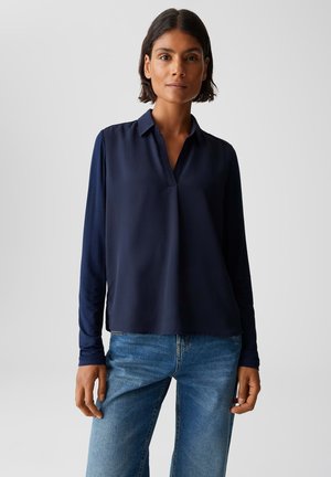 Blusa a maniche lunghe blu navy con colletto classico e vestibilità rilassata; texture morbida e orlo dritto. Abbinata a jeans azzurri.