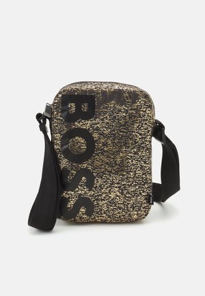 Lille rektangulær crossbody taske med sort og guld prikket mønster, sort justerbar rem og fed lodret "BOSS" tekst på forsiden.