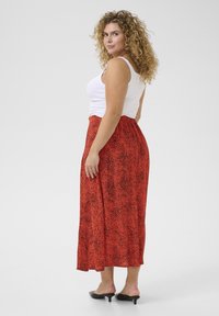 Jupe maxi à motif rouge avec une texture lisse et fluide, associée à un débardeur ajusté blanc et des mules noires à talons.