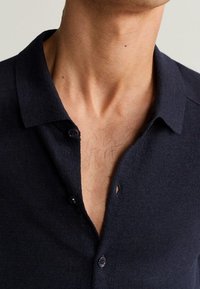 Polo in maglia blu navy con colletto, due bottoni e una piccola apertura sullo scollo. La texture appare morbida e confortevole.