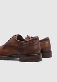 Zapatos de cuero marrón con una textura suave, que presentan una puntera redondeada, diseño de cordones y un tacón de madera apilada.