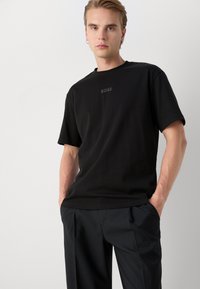 T-shirt noir à manches courtes avec un col rond et un logo "BOSS" subtil imprimé en gris foncé sur la poitrine ; tissu en coton lisse.