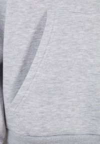 Pilka sportinė striukė su minkšta tekstūra, turinti priekinę kišenę ir raukšlėtą apdailą. Visame audinyje subtilus heather efektas.