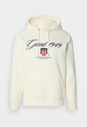 Kremna kapuca z žepom spredaj, z vrvicami in napisom "Gant 1949" nad ščitom in "American Sportswear Connecticut."