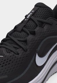 Chaussure de course Nike Winflo 12 noire avec tige en mesh, lacets noirs et logo swoosh blanc sur la semelle intermédiaire.
