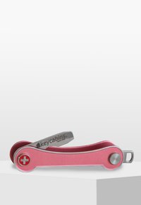 Porte-clés multi-outils en aluminium rose avec un accent métallique argenté et un logo de badge intégré. Dispose d'un design pliant unique et d'une texture lisse.