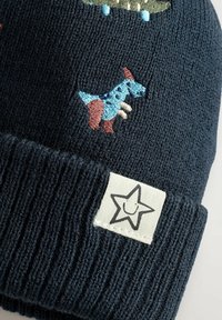 Dunkelblauer Strickbeanie mit einem gestickten blauen und braunen Hund sowie einem weißen Etikett mit einem lächelnden Sterndesign.