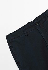 Pantaloni di cotone blu navy con una superficie liscia, dotati di chiusura con bottone frontale e passanti per cintura, ripiegati in vita.