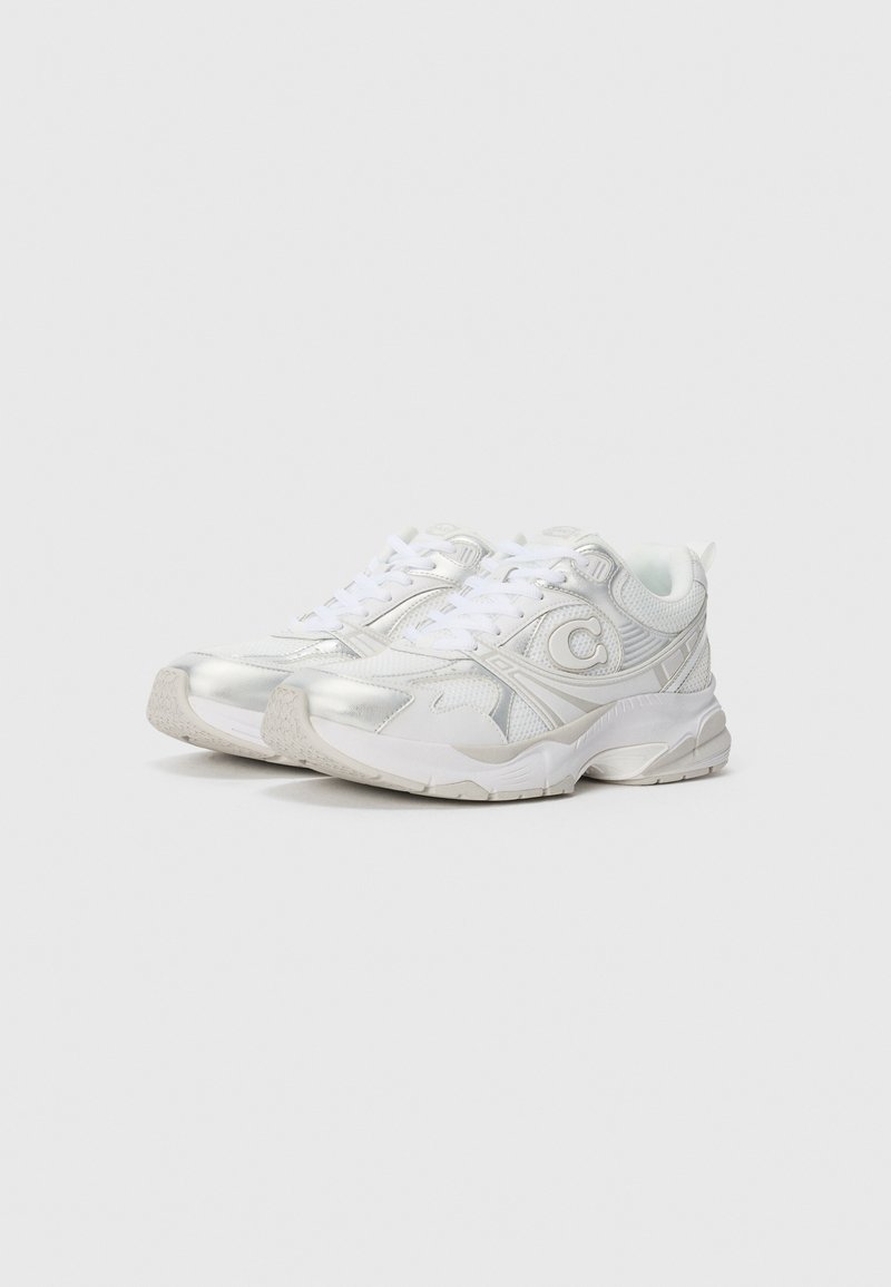 White athletic shoes with a mesh upper, metallic accents, round toe, thick rubber sole, and textured detailing on the sides.