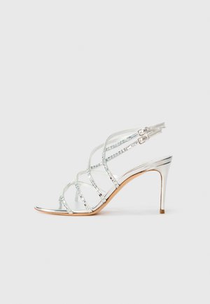 Metallic silver high-heel sandal with crisscross straps, transparent accents, and a sleek pointed toe design. Adjustable ankle buckle.