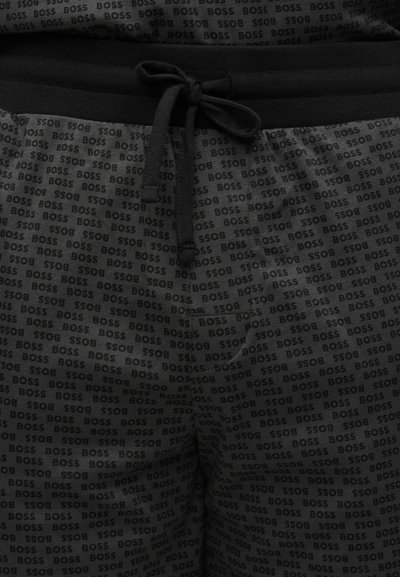 Gros plan sur un short foncé avec un cordon noir et un motif de petits textes "BOSS" sur l'ensemble, avec une poche avant côté droit.