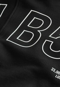 Svart sweatshirt med stora vita siffror och text, tillverkad av mjukt material, med en texturerad yta och släta tryckdetaljer.
