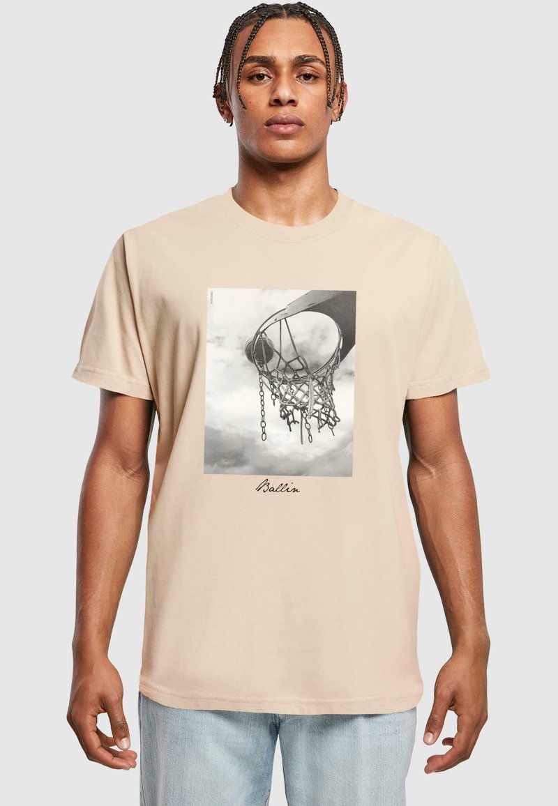 Beige bomulds t-shirt med et sort-hvidt grafisk motiv af en basketballkurv, med teksten "Ballin'" under billedet.