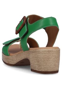 Green leather sandal with a wooden buckle, open heel, and textured beige platform. Features a smooth interior and rounded edges.