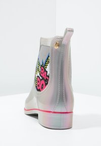 Bottes de cheville imperméables grises avec finition brillante, détail graphique éclatant présentant "BA-BOOM", et accent de semelle rose. Tirant renforcé à l'arrière pour un enfilage facile.