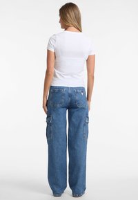 Weißes T-Shirt mit kurzen Ärmeln, kombiniert mit lässigen blauen Jeans-Cargo-Hosen, die zwei Seitentaschen und einen lockeren Schnitt haben.