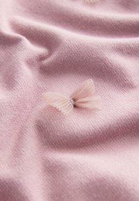 Lichtroze stof met een zachte textuur, met een delicaat tule vlinderdetail in een iets donkerdere kleur. Glad en gelijkmatig geweven.