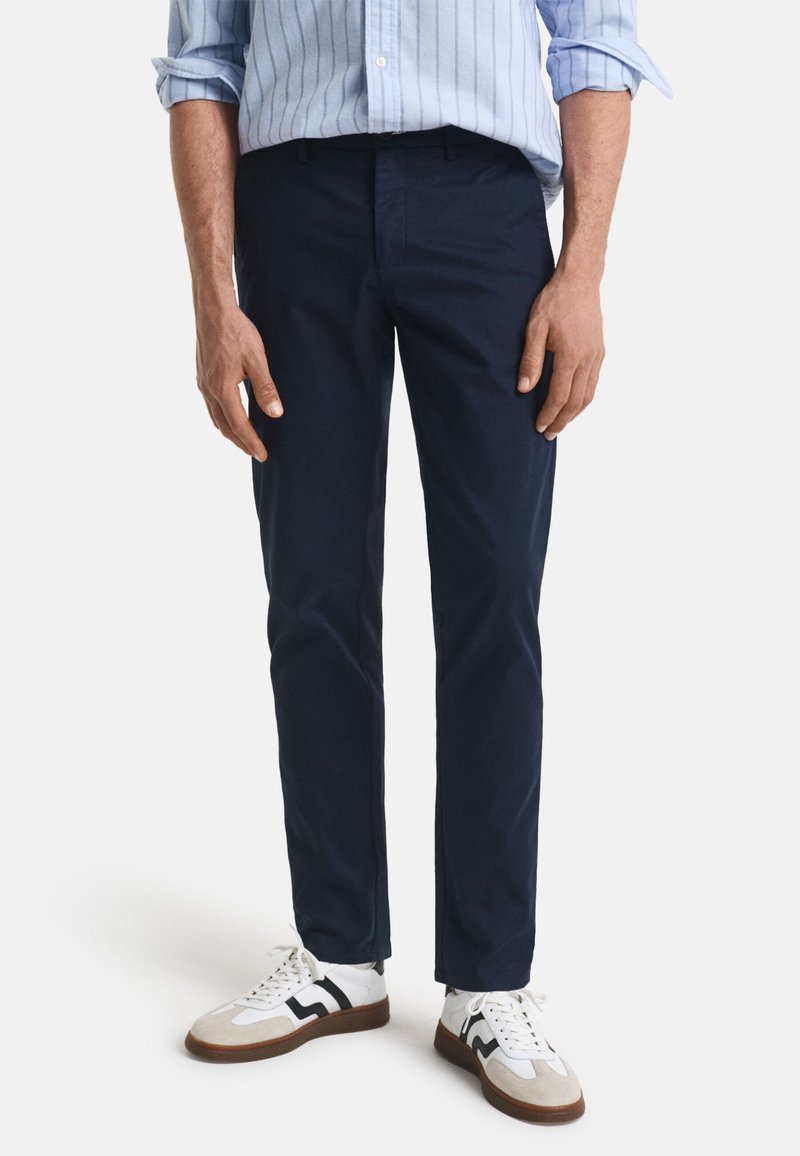 Chinos bleu marine à coupe droite, confectionnés en coton, associés à des baskets blanches avec des accents noirs et une semelle marron.
