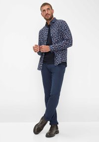 Blauwe bloemenlange mouw blouse met een zwarte ronde hals erboven, gecombineerd met marineblauwe chino's en donkerbruine laarzen.