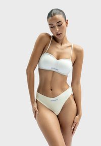 Witte bh en bijpassende bikini onderkant met dunne bandjes, gladde textuur en logo detail. Eenvoudig ontwerp met een nauwsluitende silhouet.