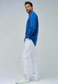 Hellblauses Langarmhemd mit knopfbaren Manschetten, kombiniert mit weißen Slim-Fit-Hosen und weißen Sneakers. Einfaches, klares Design mit minimalen Details.