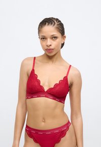Roter Spitzen-Bralette und passender Tanga mit dünnen Trägern. Der Bralette zeichnet sich durch gezackte Ränder und ein gebrandetes elastisches Band unter der Brust aus.