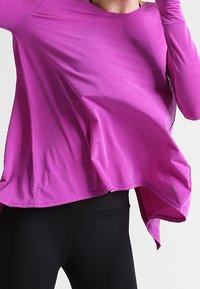 Lätt, långärmad träningströja i en livfull magenta färg, med löst snitt, rundad halsringning och svängd nederkant. Matchas med svarta leggings.