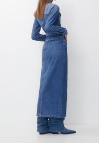 Denimskjolklänning i ljusblått, lång och figursydd med långa ärmar, har midjeband och sidoremsor. Kombinerad med blåa avslappnade ankelskor.