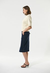 Strikket cremefarvet kortærmet sweater med tekstureret detalje, parret med en knælang mørkeblå nederdel med sidelommer og kontrasterende syninger.