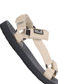 Beige Jack Wolfskin sandal with black sole and adjustable fabric straps secured by Velcro closures.