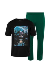 Zwarte t-shirt met een kleurrijke afbeelding van een wolf en een astronaut, gecombineerd met plain groene joggingbroek, beide in een casual pasvorm.