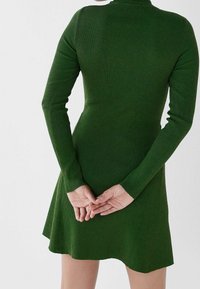 Robe longue à manches longues verte à côtes avec un corsage ajusté, une jupe évasée et un col montant. Tissu texturé et détails discrets au dos.