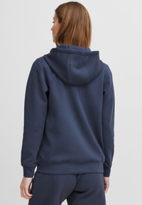 Felpa blu navy con cappuccio, realizzata in materiale morbido. Presenta polsini e orlo a coste, con una texture liscia e senza decorazioni visibili.