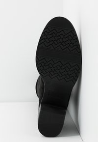 Semelle d'une chaussure noire avec un motif de bande de roulement en zigzag et en chevrons, présentée sur une surface blanche en angle.