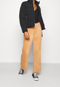 Czarna kurtka puchowa z zamkami, w połączeniu z jasnoróżowymi sztruksowymi spodniami typu wide-leg i czarnymi wysokimi trampkami.