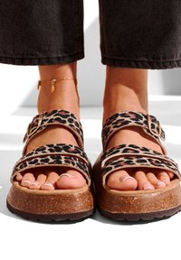 Leopard print sandals with two wide straps, buckles, cork footbed, and textured sole. Features open toe and a flat design for comfort.