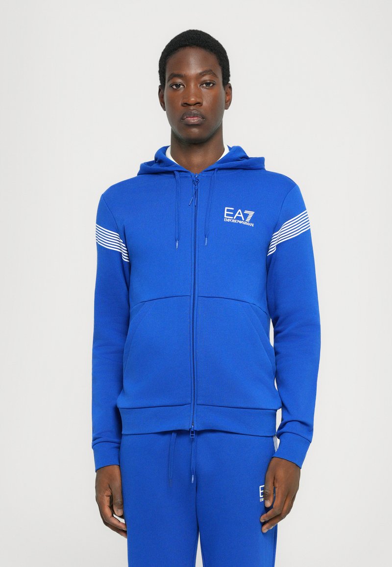 Royal blå zip-up hettegenser i mykt stoff, med en frontlomme, hvite stripeakenter på skuldrene, og EA7-logo på brystet.