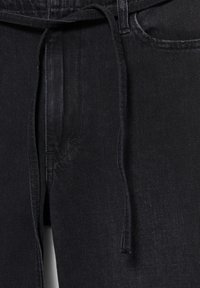 Schwarze Jeans aus Denim mit einem vorne gebundenen Stoffgürtel, Nahaufnahme des Bund- und Taschenbereichs vorne.