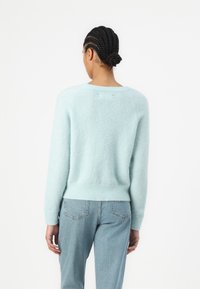 Lyseblå, lodden strikkegenser med rund hals, ribbestrikkede ermer og nederkant. Har en avslappet passform og subtil tekstur. Brukes med lyse jeans.