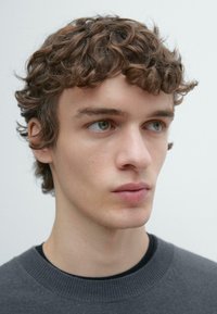 Gray sweater with a ribbed neckline, featuring a model with short, curly brown hair and clear skin, against a plain white background.