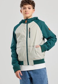 Giacca da uomo colorblock in beige e verde scuro, con zip frontale, cappuccio, polsini elasticizzati e una tasca sul petto con una zip arancione.