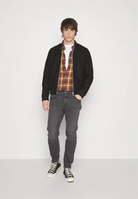 Geacă bomber neagră, cămașă în carouri galbenă și burgundă, tricou alb, blugi gri și adidași negri cu tălpi albe.