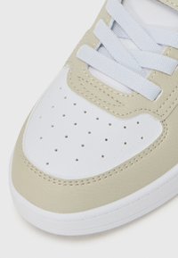 Baskets gris clair et blanches avec une tige en cuir texturé, un bout perforé, des lacets blancs plats et une semelle rembourrée.
